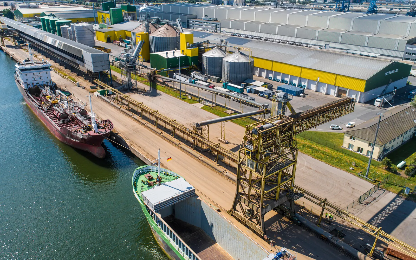 Luftaufnahme eines Werks am Hafen mit Schiff an der Kaikante