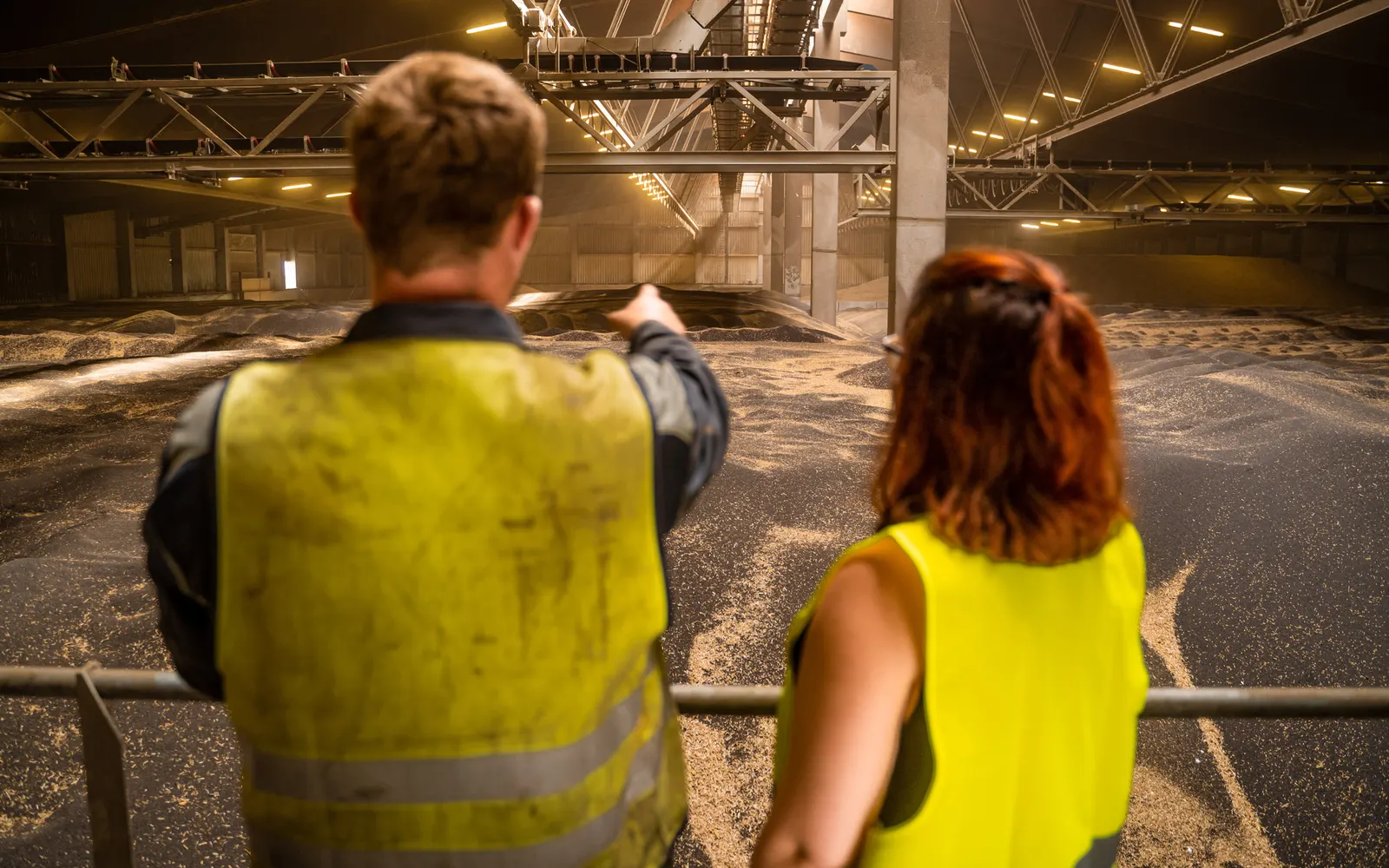 Industriefotografie: zwei Mitarbeitende in Warnwesten blicken in eine große Lagerhalle