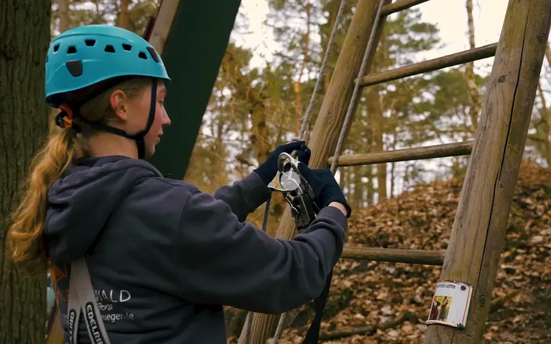 Gedrehter Erklärfilm: eine Kletterin sichert sich im Kletterwald